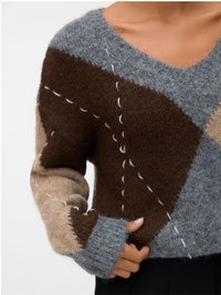 Sweter dziergany w szarościach, brązach i beżach. Posiada dekolt w serek, wzór patchworkowy oraz kontrastowe przeszycia. Miękka tekstura, luźny krój.
