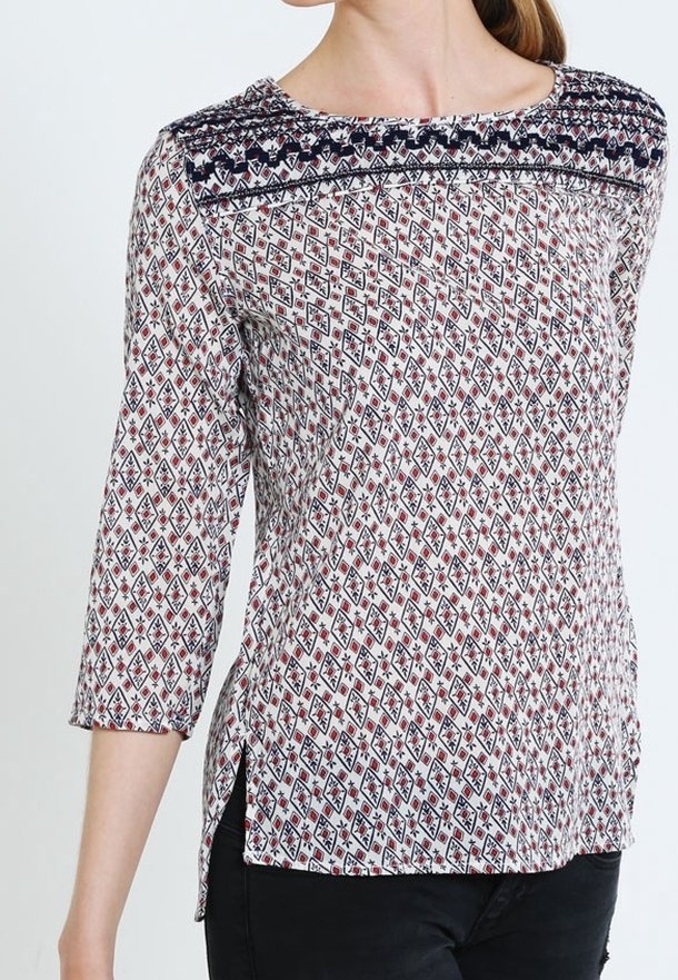 Blouse à manches longues avec un motif géométrique rouge, marine et blanc, ornée d'un col brodé marine et de fentes latérales pour faciliter les mouvements.