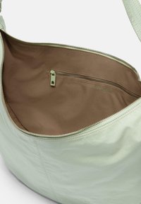 Borsa a spalla verde menta realizzata in materiale morbido. Interno foderato in tessuto marrone con una tasca con zip. Chiusura con cerniera argentata.