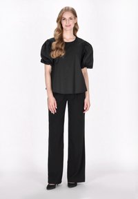 Sort puffærmet top kombineret med sorte højtaljede, vide bukser. Glat stof med en afslappet pasform og en subtil glans. Sorte sko afslutter outfittet.