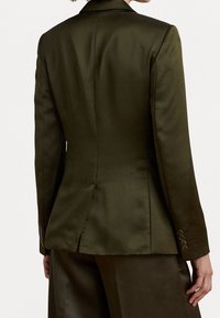 Světlý olivově zelený saténový blazer s přiléhavým designem, s jedním rozparkem a knoflíkovými manžetami. Hladký povrch a zúžený silueta. Žádné viditelné kovové prvky.