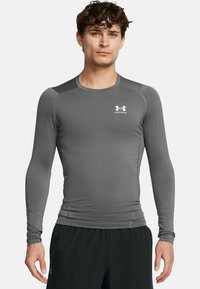 Graues langärmliges Sportshirt mit rundem Ausschnitt, tailliertem Schnitt und dem weißen Under Armour-Logo auf der Brust. Glatte Textur.