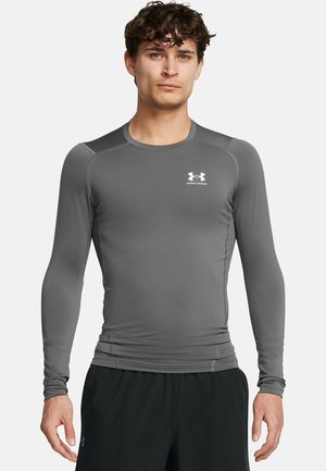 Grå langærmet træningsskjorte med rund halsudskæring, tætsiddende design og Under Armour-logoet i hvidt på brystet. Glat tekstur.