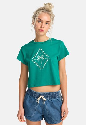 Zielona krótka koszulka z bawełny z białym nadrukiem palmy w kształcie diamentu. Połączona z dżinsowymi szortami z paskiem w talii.