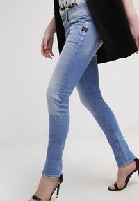 Jeans ajustados de denim de color azul claro, con un lavado medio, una cintura a media altura y un ligero desgaste en los muslos. Se combinan con tacones negros.