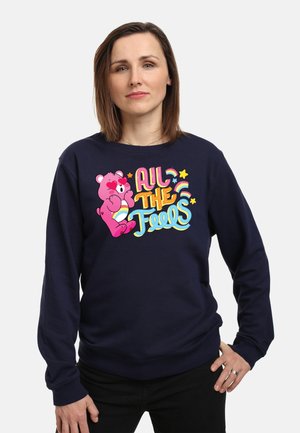 Mørkeblå sweatshirt med et farverigt grafik af en pink bjørn og teksten "All the Feels" i legende typografi. Blødt bomuldsblanding materiale.