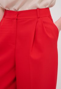 Rode op maat gemaakte broeken met een hoge taille, plooien en zijzakken. Gemaakt van zachte stof met een schone, gestructureerde silhouette.