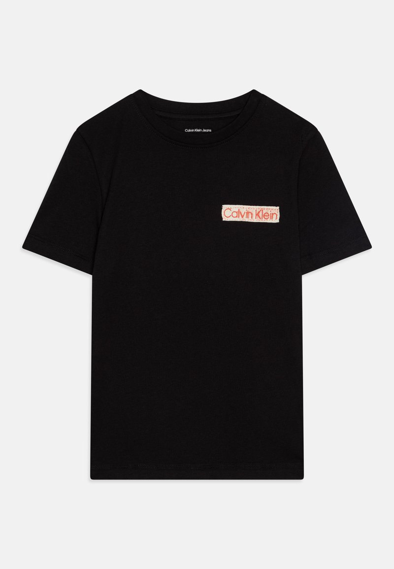 Camiseta de algodón negra con mangas cortas. Presenta una etiqueta blanca con el texto rojo "Calvin Klein" en el área del lado izquierdo del pecho. Diseño simple con cuello redondo.