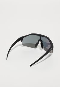 Black sports sunglasses with angular frame, gray tinted lenses, rubber nose pads, and thin black arms featuring logo on the side.