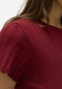 Top en tricot rouge avec un motif en relief et un col en dentelle. Le tissu présente un motif subtil avec des manches courtes.