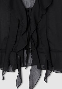 Tessuto nero trasparente con bordi a strati e volant, e lacci coulisse, creando un dettaglio di un indumento fluido e texturizzato su uno sfondo chiaro.