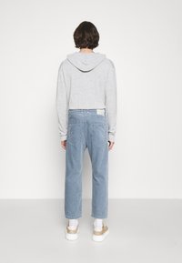Felpa grigia con cappuccio e maniche lunghe, abbinata a pantaloni a vita alta in velluto a coste a righe blu chiaro e sneakers beige. Vista posteriore mostrata.