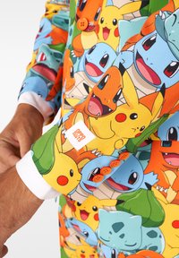 Kleurrijke colbert met cartoon Pokémon-figuren, gemaakt van stof met een soepele textuur; oranje knopen en een witte manchet voegen detail toe.