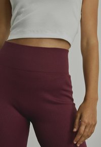 Rebrasti bordo tajice visokog struka s glatkom teksturom. Nosive uz uski bijeli crop top, prikazujući istančan siluet.