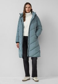 Hellblauer, gesteppten Pufferjacke mit Kapuze, Reißverschluss und gerippten Bündchen, kombiniert mit einem weißen Strickpullover und dunklen Jeans, entworfen für Wärme.