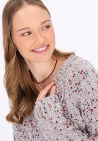 Pulover gri deschis cu stropi multicolori, textură groasă și croială lejeră. Însoțit de un colier roșu din mărgele cu un pandantiv mic.