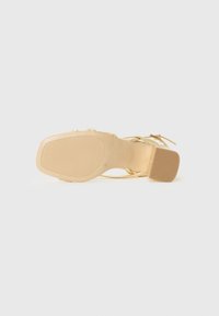 Golden high-heeled sandal with a textured sole, slender straps, and a wide, rectangular block heel. Smooth finish with minimal accents.