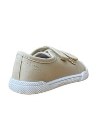 Zapatillas de lona beige con tiras de Velcro, punta redondeada y suela de goma blanca. Presenta un agarre texturizado en la suela y un lado con la marca.