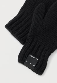 Čierne pletené rukavice s žíhanou textúrou, zúženými končekmi prstov a obdĺžnikovou štítkom s bielym textom na manžete.