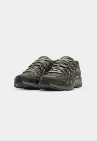 Nike sneakers in olive green with mesh panels and maroon accents. Features textured soles, rounded toe, and lace-up front.