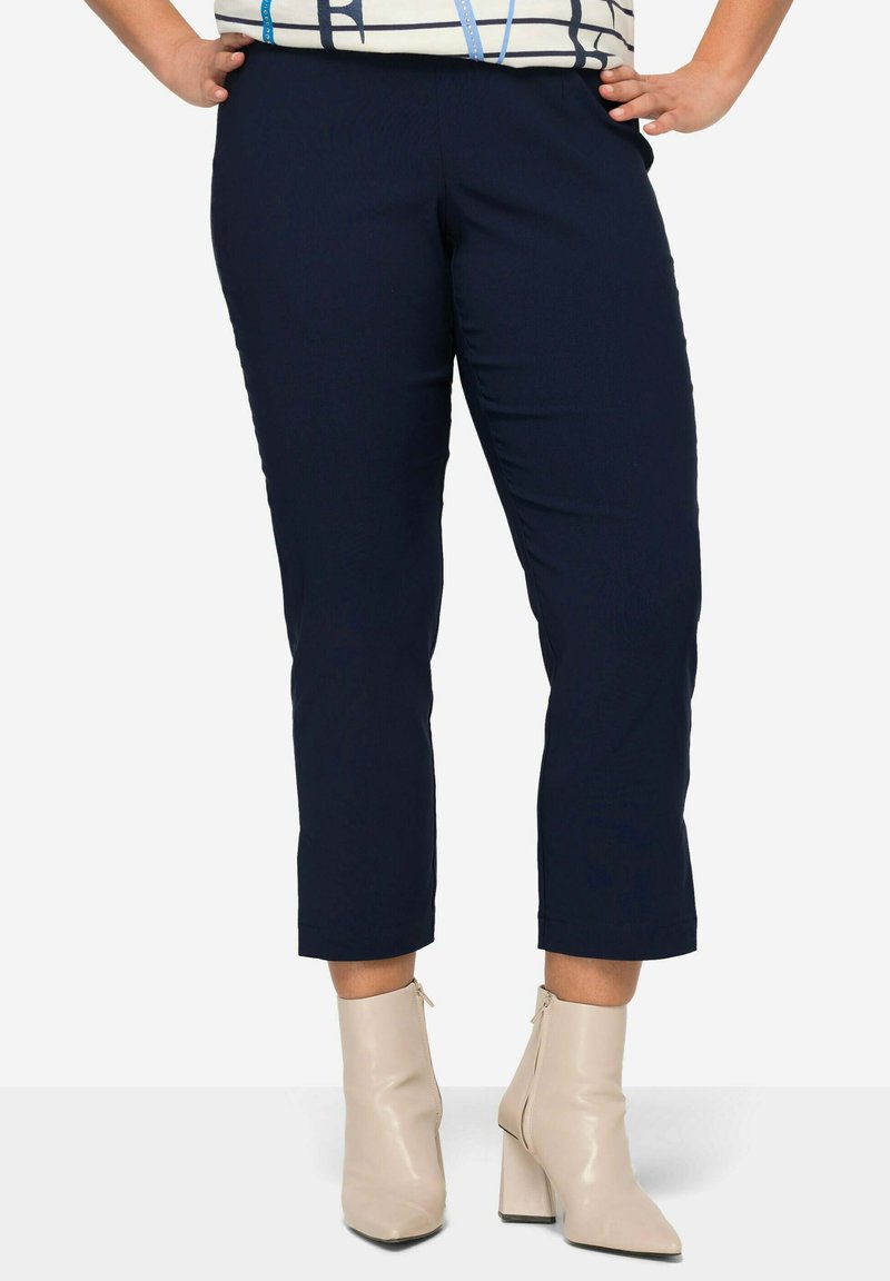 Navy-blaue, cropped Hosen mit geradem Schnitt, ausgestattet mit einer glatten Textur und einem elastischen Bund, kombiniert mit cremefarbenen Stiefeletten.