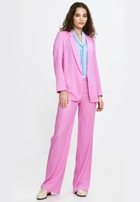 Różowy garnitur skrojony z długim żakietem i szerokimi spodniami, w połączeniu z jasnoniebieską bluzką. Gładka tekstura i zorganizowany krój.