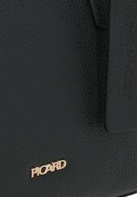 El bolso de mano de cuero negro texturizado presenta un logo dorado "PICARD", una etiqueta suave con el grabado "SINCE 1928" y sencillos acentos de hardware.