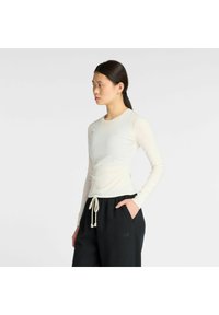Lichtbeige langharige top met een aansluitend ontwerp en een gladde textuur, gecombineerd met donkere joggingsbroeken met een elastische tailleband en broekkoord.