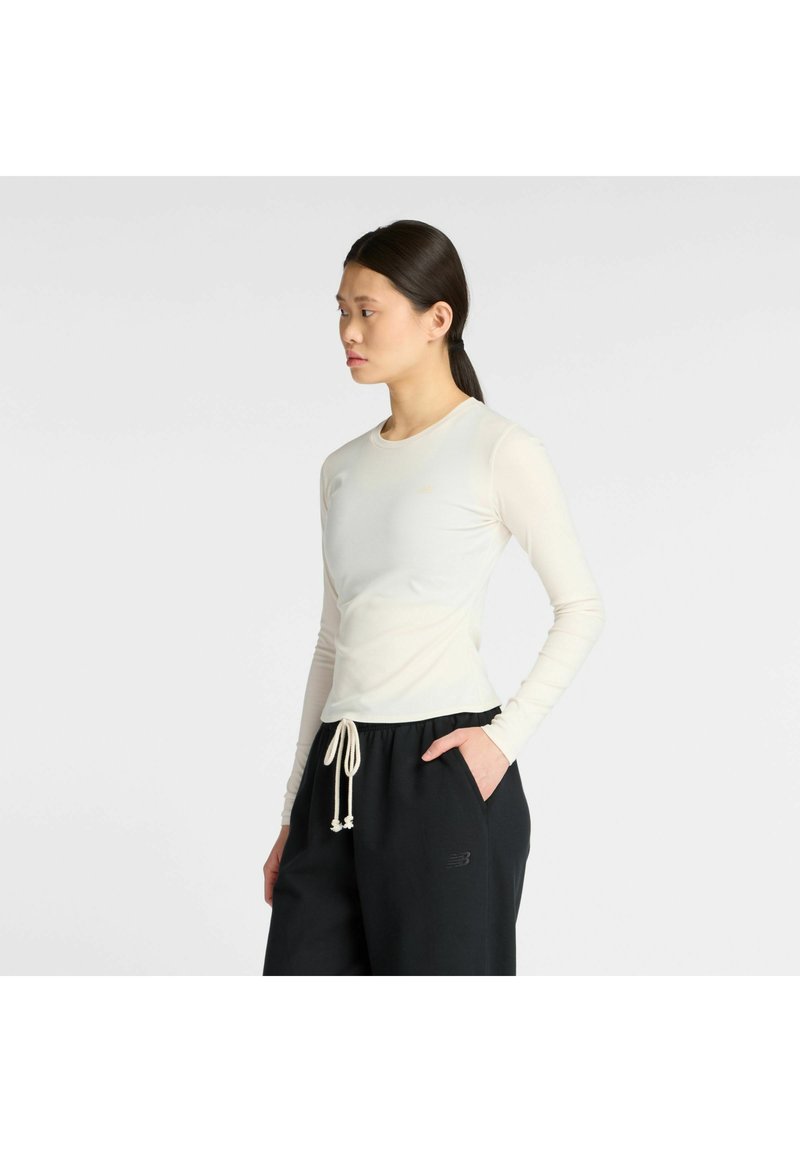 Lichtbeige langharige top met een aansluitend ontwerp en een gladde textuur, gecombineerd met donkere joggingsbroeken met een elastische tailleband en broekkoord.
