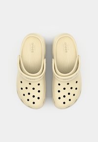 Sabots Crocs beige avec un design perforé, une bride arrière et une semelle intérieure texturée. Fabriqués en matériau léger pour le confort.