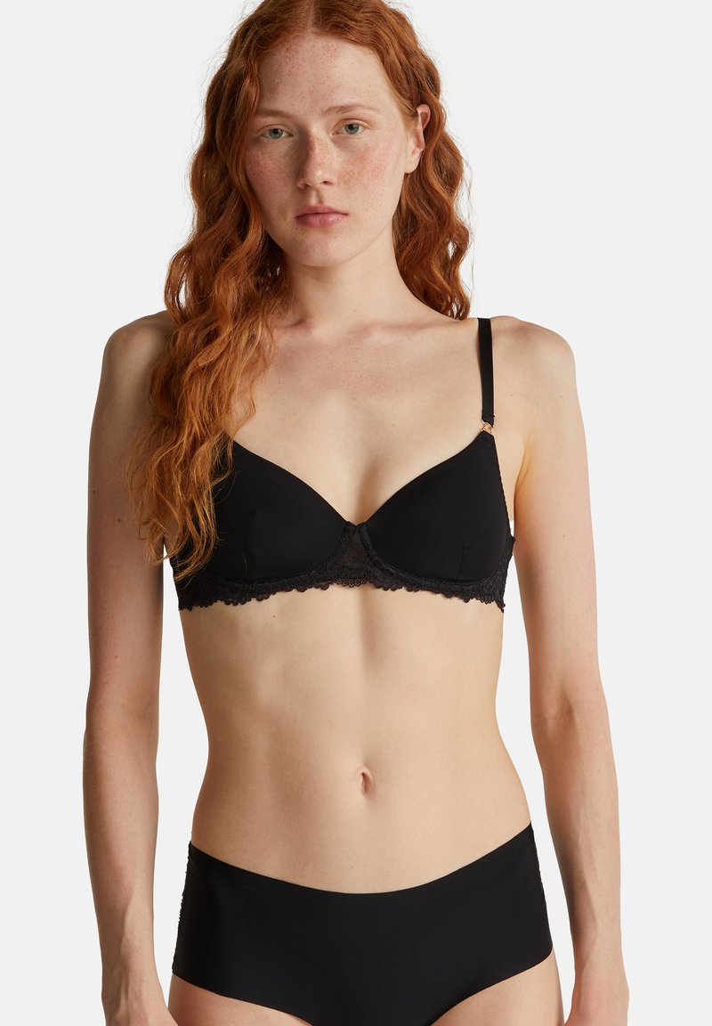 Černá podprsenka s hladkými košíčky a krajkovým lemem na spodní části, nastavitelnými ramínky a zapínáním na háček a očko na zadní straně.