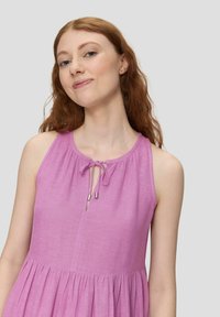 Lavendelfarbenes ärmelloses Kleid mit rundem Ausschnitt, das ein Kordelzugdetail auf der Vorderseite und einen fließenden, plissierten Rock bietet. Glatte Textur.