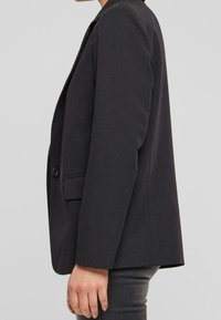 Czarny żakiet wykonany z gładkiej tkaniny, z dwoma guzikami, pojedynczą kieszenią na piersi i wyraźnie zarysowanymi ramionami, pokazany z boku.