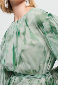 Sheer green dress featuring a pleated design, cinched waist with a matching belt, and subtle texture with layered fabric.