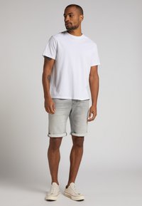 Camiseta blanca de algodón, de manga corta y cuello redondo; combinada con shorts de mezclilla gris claro, con dobladillo. Llevada con zapatillas de deporte color blanco roto.