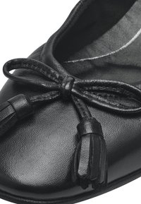 Ballerine in pelle nera con punta arrotondata, un dettaglio a fiocco con frange nella parte frontale e una superficie liscia e strutturata.
