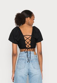 Top preto curto com mangas bufantes e costas com cordão, combinado com jeans de denim azul claro de cintura alta. Tecido suave, estilo casual.