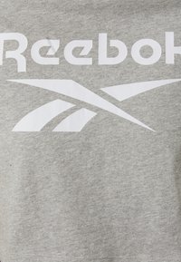 Grå bomulls T-skjorte med stort hvitt "Reebok"-logo og stilisert grafisk design. Myk tekstur, rund hals, korte ermer.
