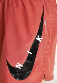 Rode sportieve shorts van gladde stof met een elastische tailleband. Heeft een groot zwart Nike-swoosh en witte letters aan de zijkant.