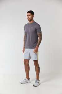 Grå kortermet treningsskjorte med logo, kombinert med lysegrå shorts med gult detalj. Brukt sammen med grå og hvite treningssko.