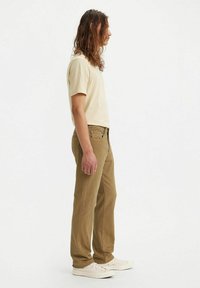 Beige t-shirt, bruine jeans en witte sneakers. De jeans hebben een rechte snit en subtiele stiksels. Lichtgewicht stof met een gladde textuur.