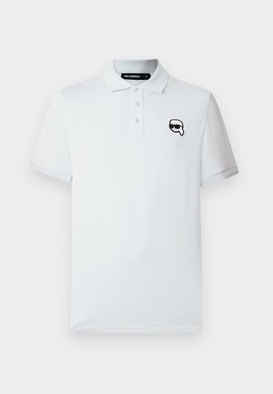 Bijela polo majica kratkih rukava s tri gumba i malim crno-bijelim crtežom lica u sunčanim naočalama na lijevoj strani prsnog koša.