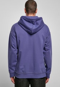 Kapucnis pulóver sötétlila anyagból, laza szabással, bordás mandzsettákkal és enyhén hosszabb hátfennel.