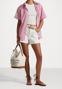 Camicia a righe rosa con bottoni, canotta bianca, pantaloni shorts bianchi tagliati, cintura testurizzata, sandali marroni e borsa in tela con design grafico.