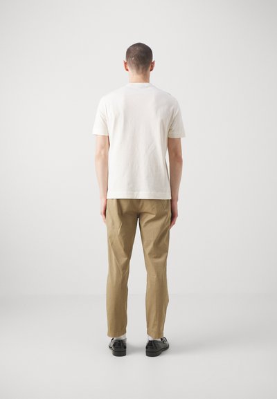 T-shirt en coton blanc à manches courtes, associé à un pantalon marron clair. Le pantalon présente une texture lisse et une coupe ajustée.