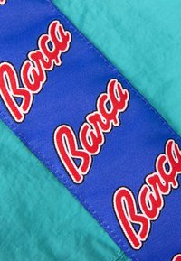 Blauwe stof met herhalende "Barça" tekst in het rood. Geplaatst op teal materiaal, toont een gladde textuur en contrasterende kleuren.