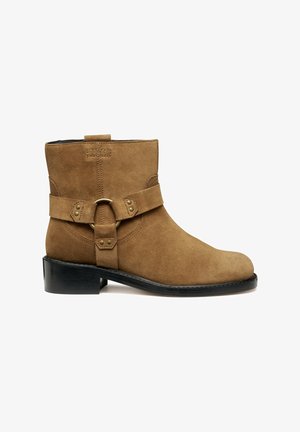 Bottine en daim beige avec un bout rond, une bride décorative avec boucle, et un petit talon empilé noir.