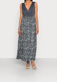 Sukienka maxi z głębokim dekoltem w serek, bez rękawów, ciemnoszara góra oraz spódnica w wzory z zielonymi i różowymi liśćmi. Gładki materiał.