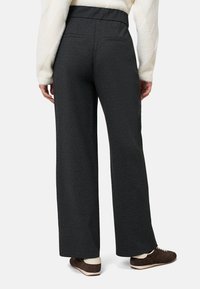 Donkergrijze wijde broekspijpen gemaakt van gestructureerde stof, met een hoge tailleband en twee achterzakken, gecombineerd met bruine sportschoenen.