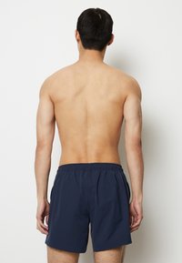 Pantaloni da bagno blu navy con elastico in vita, tasche laterali e tessuto leggero e ad asciugatura rapida. Vista da dietro.